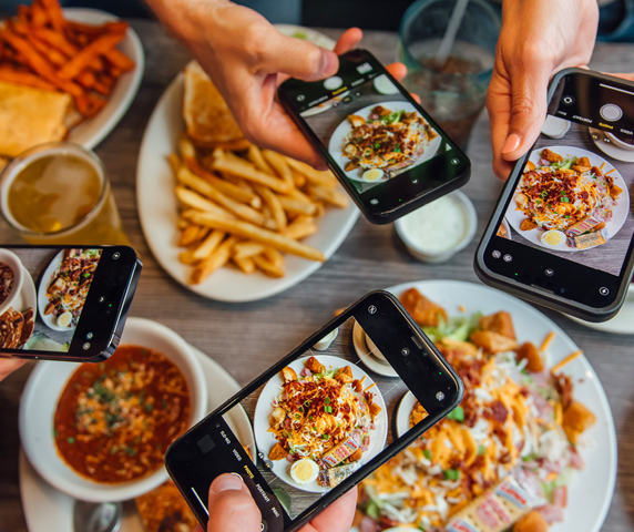 A bunch of phones taking photos of Brew Bacher's food items for social media.