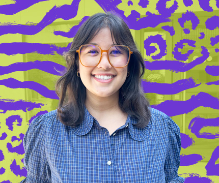 Portrait of a smiling woman with orange-rimmed glasses and a blue checkered shirt, against a bright lime-green and purple abstract background.